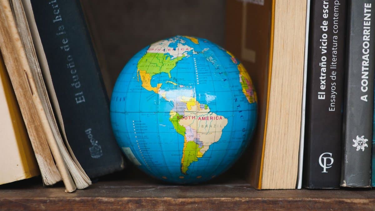 A vibrant globe nestled between classic books on a wooden shelf, highlighting South America.