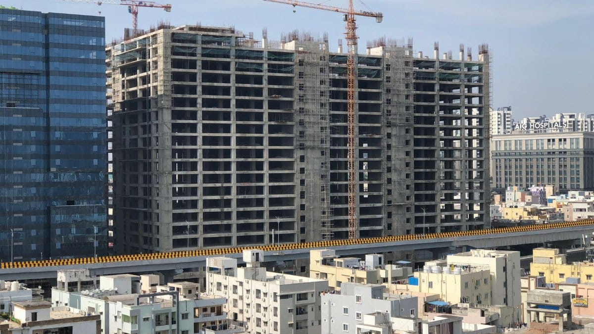 High-rise building under construction in a bustling city with cranes and urban infrastructure.