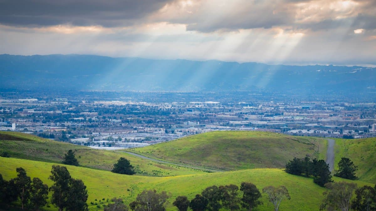 Breathtaking view of green hills with sun rays over a town in the valley.