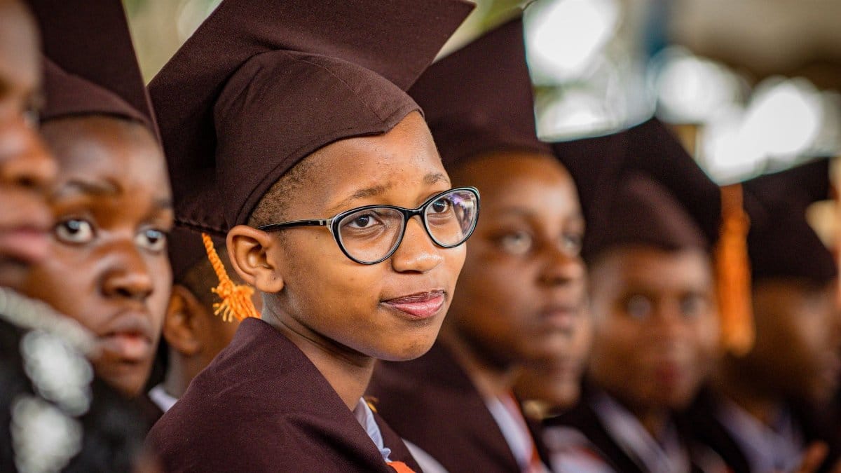 A group of young graduates in caps and gowns attentively participate in a ceremony.
