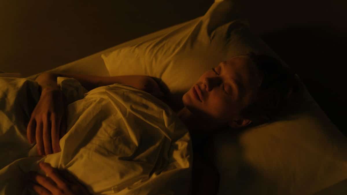 A woman peacefully sleeping in a dimly lit bedroom, wrapped in a white blanket.