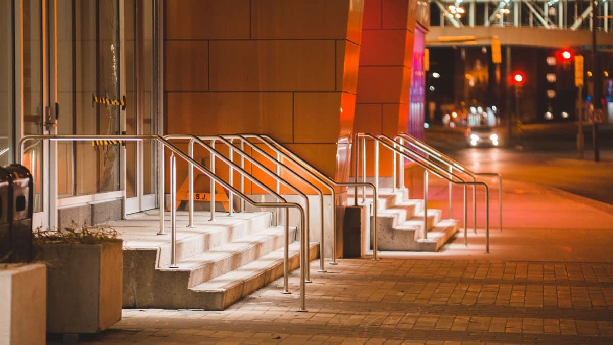 Shiny stairs of modern building near tiled sidewalk and road with car in city at dusk