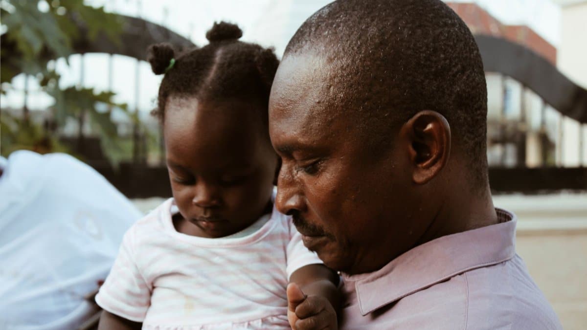 A father holds his young daughter lovingly outdoors. A display of family and togetherness.