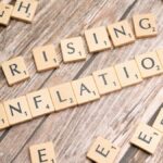 Wooden letter tiles spell 'rising inflation' symbolizing economic concerns.