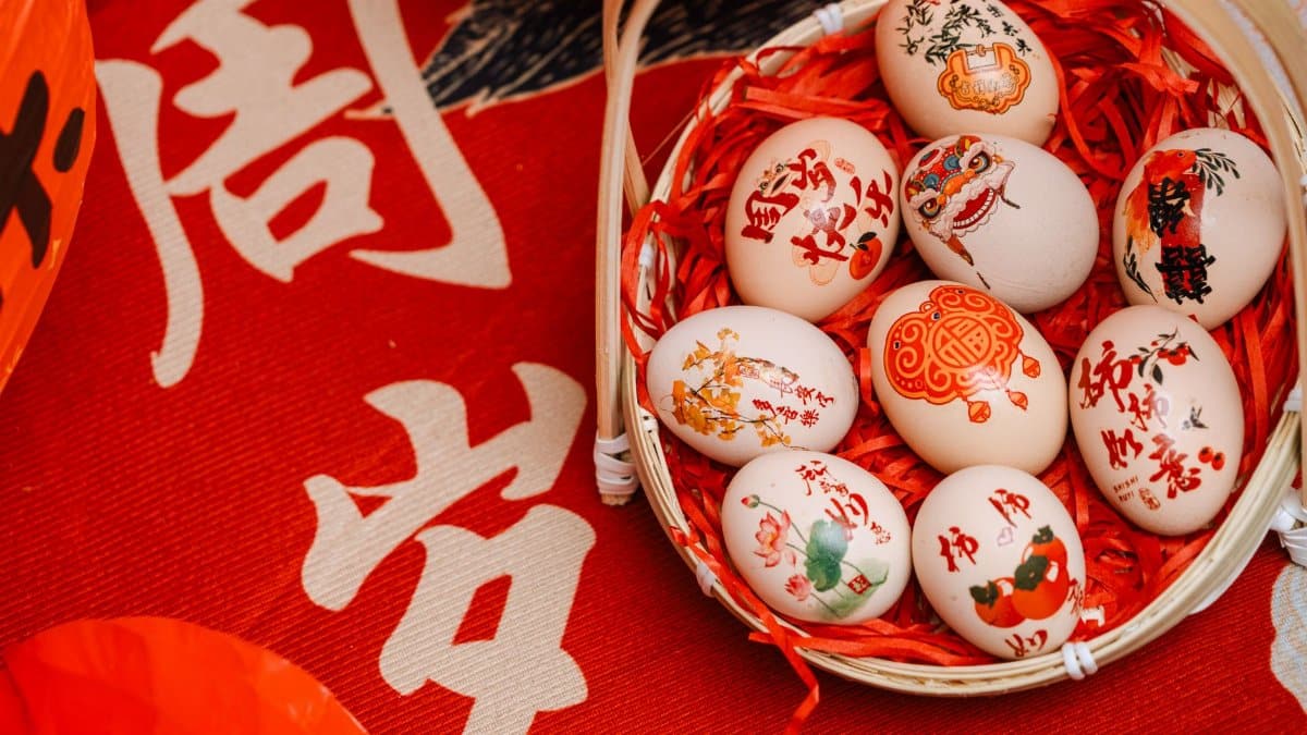 Basket of ornately decorated eggs for Chinese New Year on a vibrant red background with Chinese calligraphy.