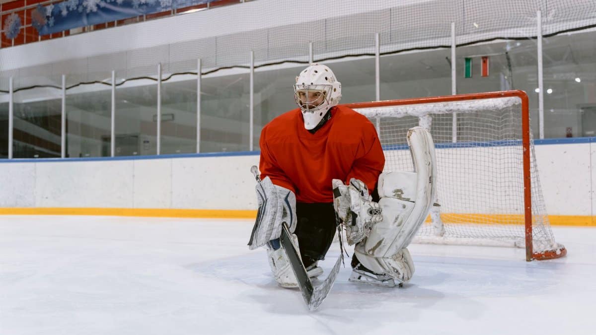 Ice hockey goaltender in red jersey at the rink, ready to defend the goal.