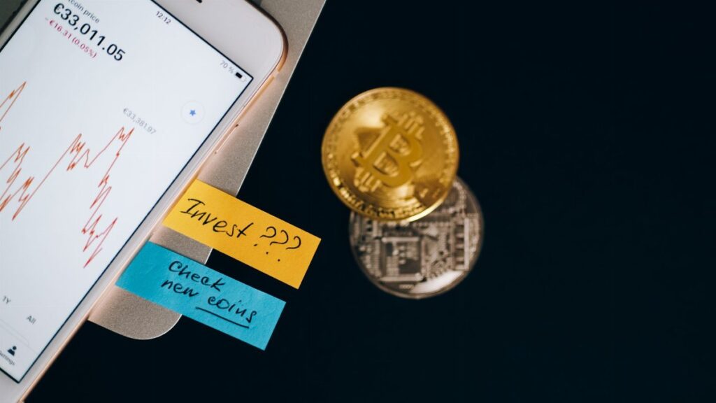 Bitcoin coins and smartphone displaying price chart with investment notes.