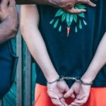 Close-up of a handcuffed person under arrest by a police officer outdoors.