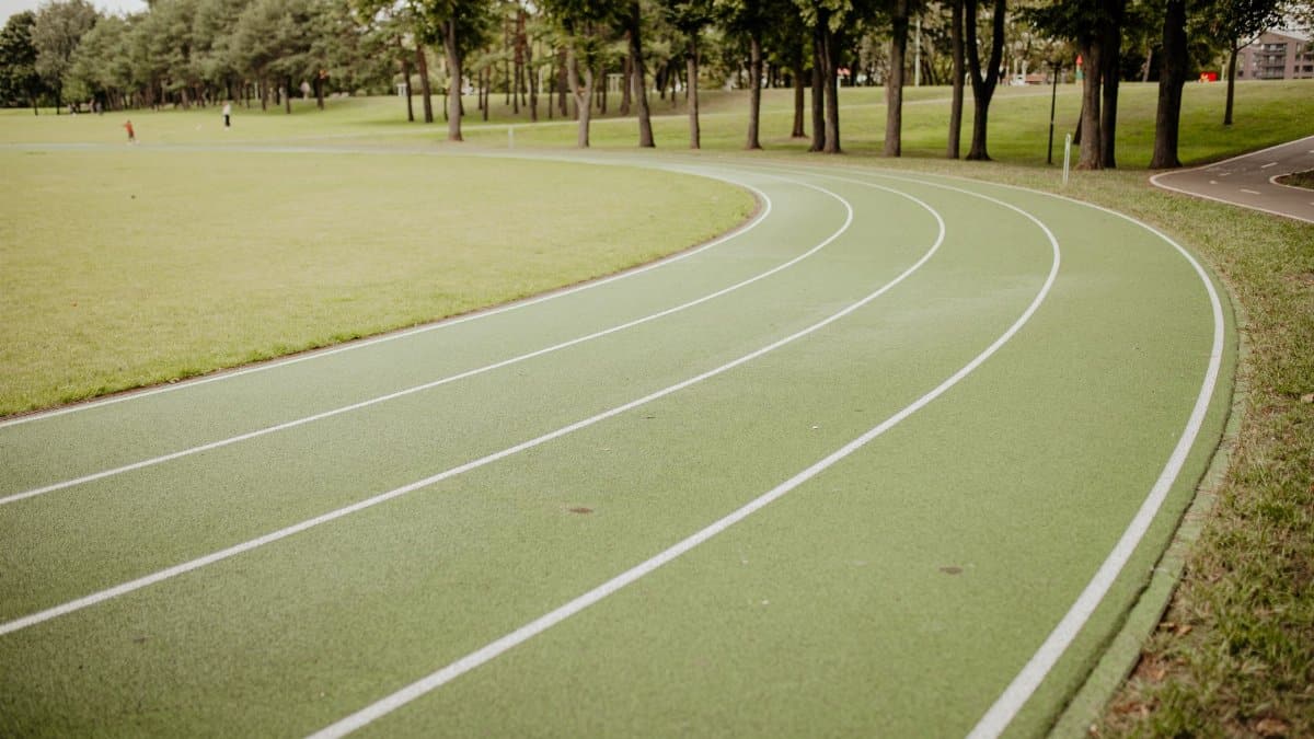 A curved green running track in a lush park setting under bright daylight.