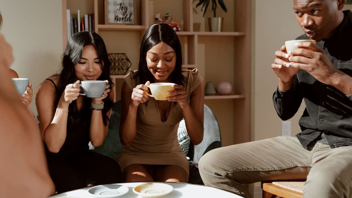 Group of friends laughing and bonding over hot drinks in a welcoming café interior.