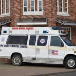 Old King County Medical Service ambulance parked beside a brick building on a street corner.