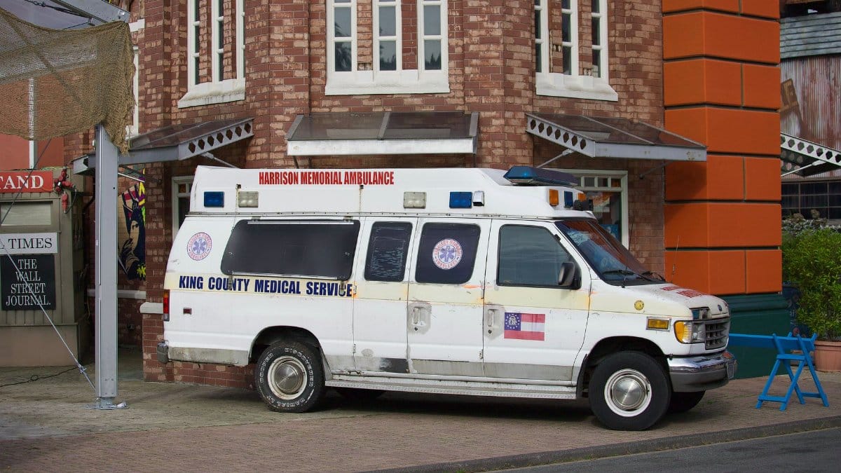 Old King County Medical Service ambulance parked beside a brick building on a street corner.