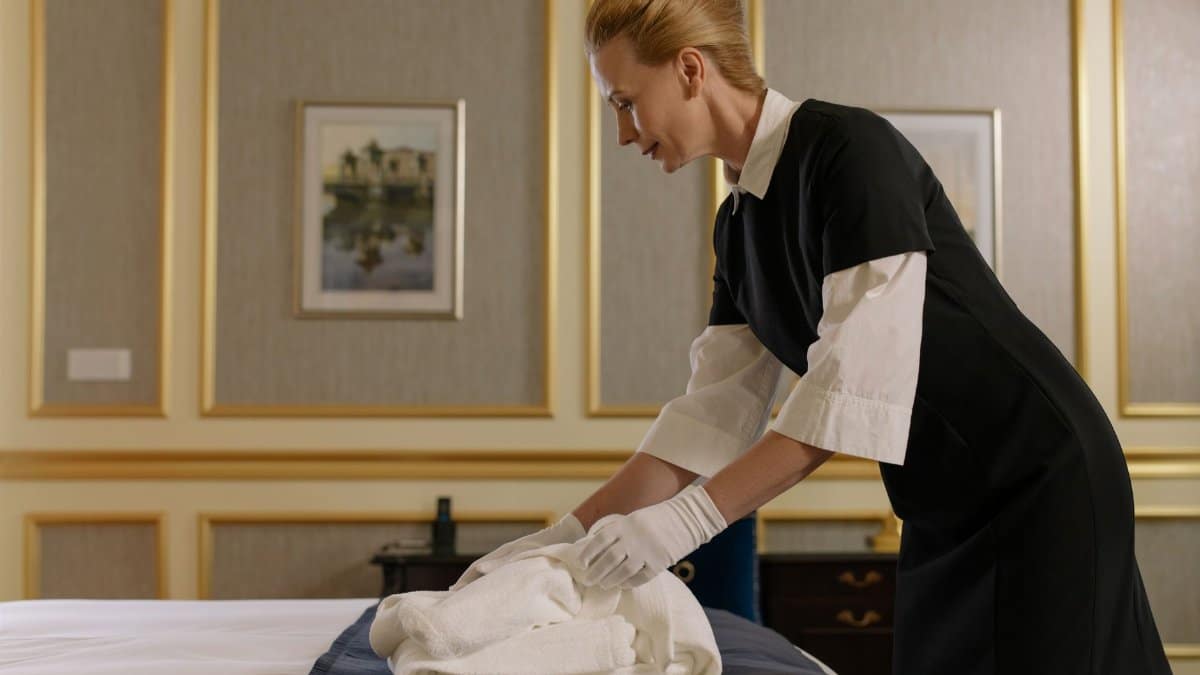 A housekeeper neatly folds sheets on a luxury hotel bed, emphasizing professional service.