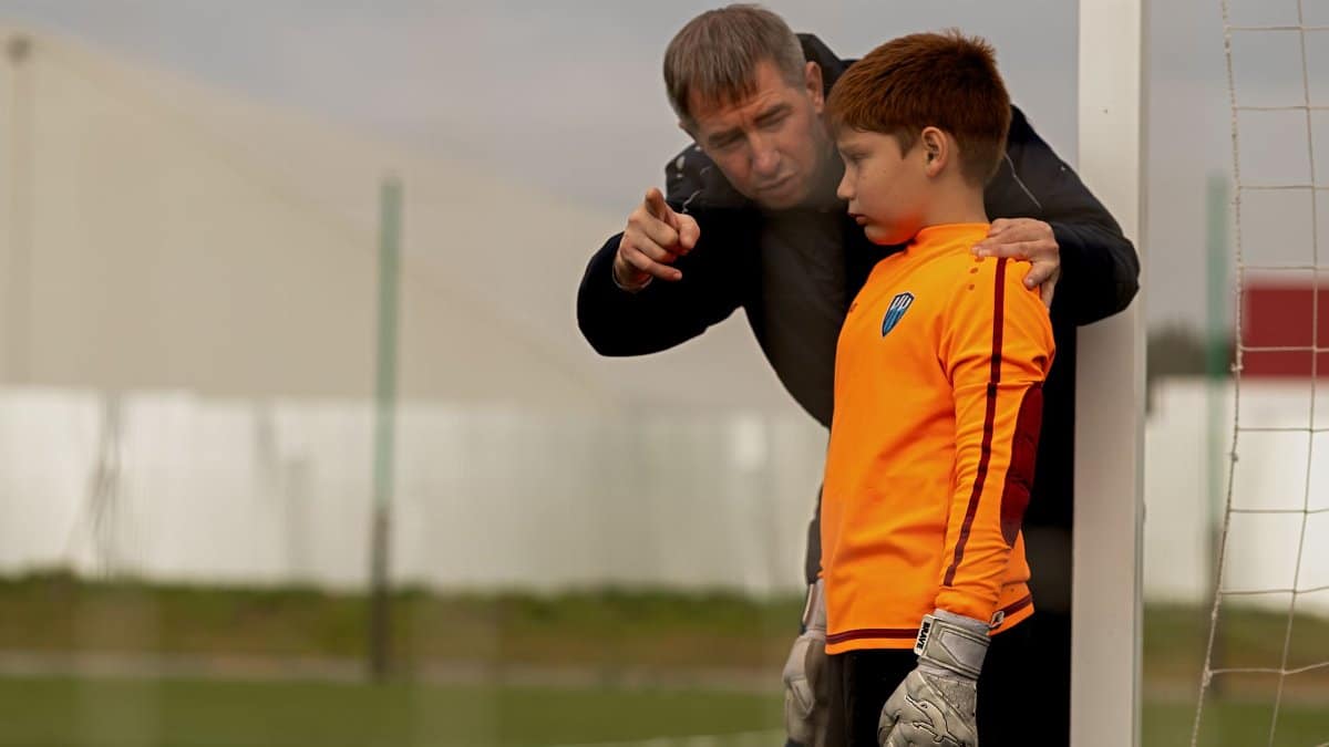 A coach providing guidance to a young goalkeeper on a soccer field.