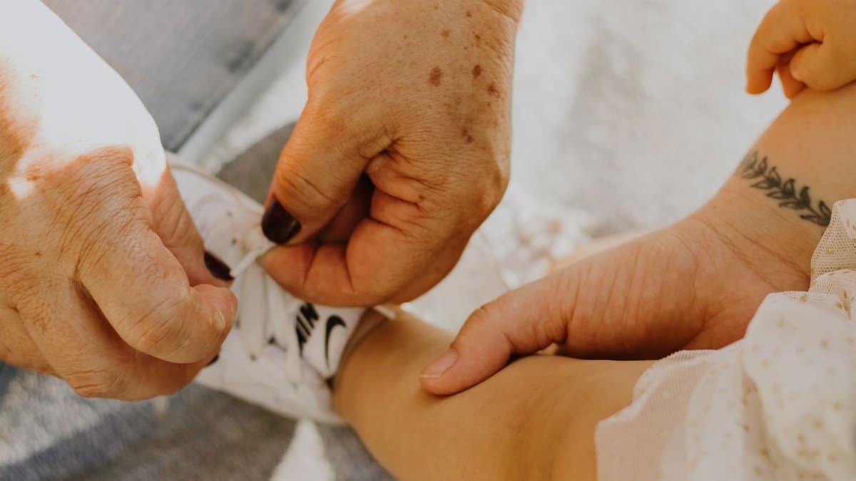 An elderly woman helps tie a baby's Nike shoe, highlighting care and intergenerational bonding.