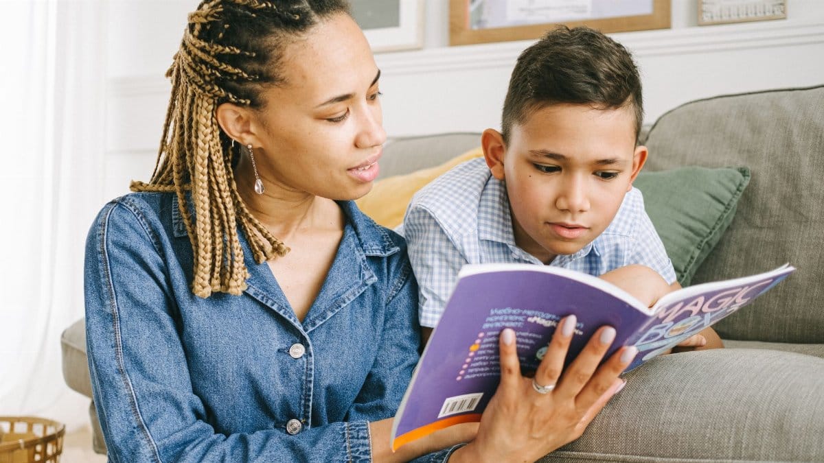A mother reading a book with her young son on a comfortable couch indoors.