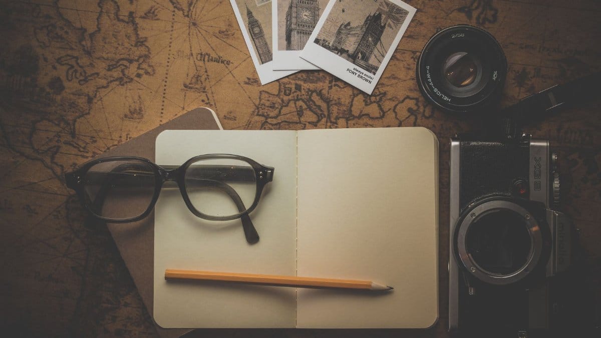 Flat lay of travel essentials including camera, notebook, eyeglasses, and map for adventure planning.