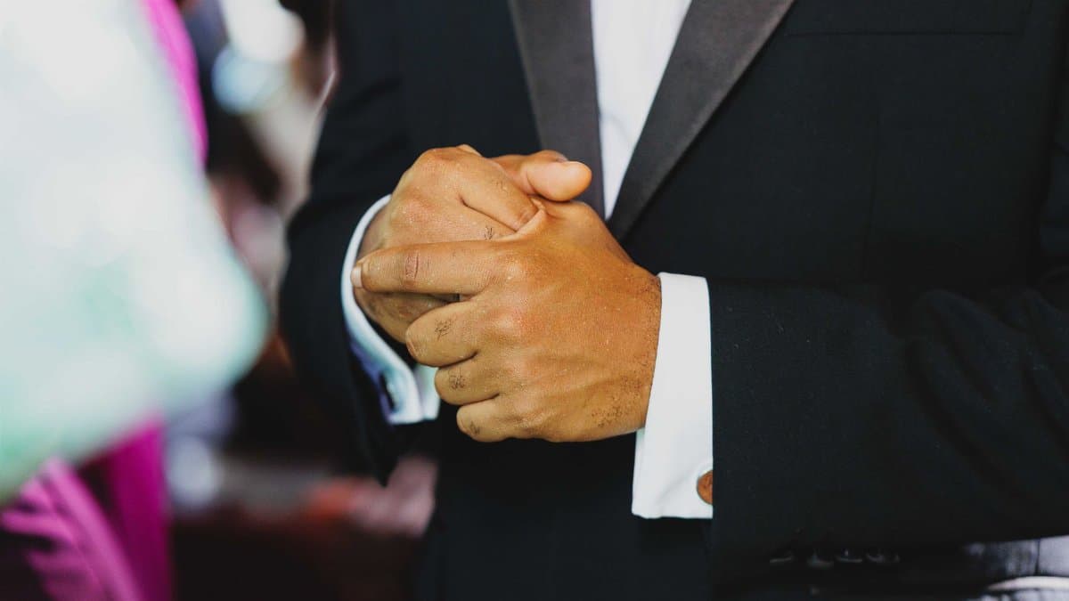 Close-up of a man clasping his hands in a black tuxedo at an event, showcasing elegance and sophistication.