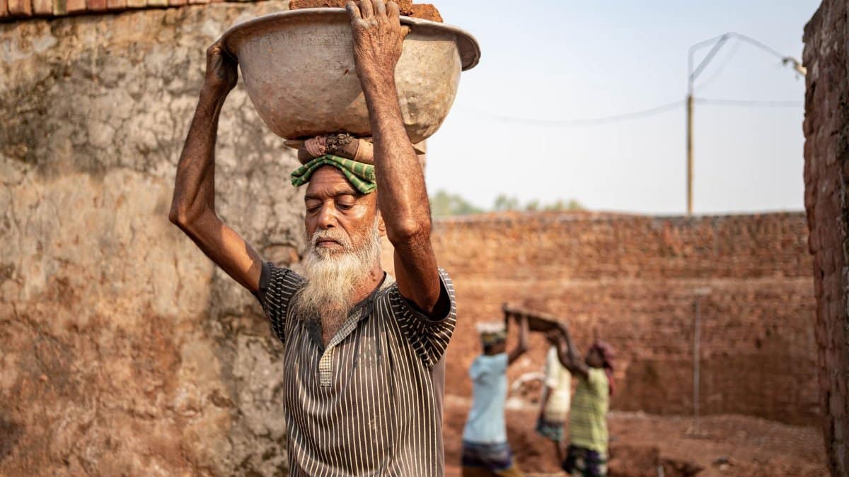An elderly man carrying bricks at a Dhaka brickfield, illustrating the hard work and struggle of laborers.