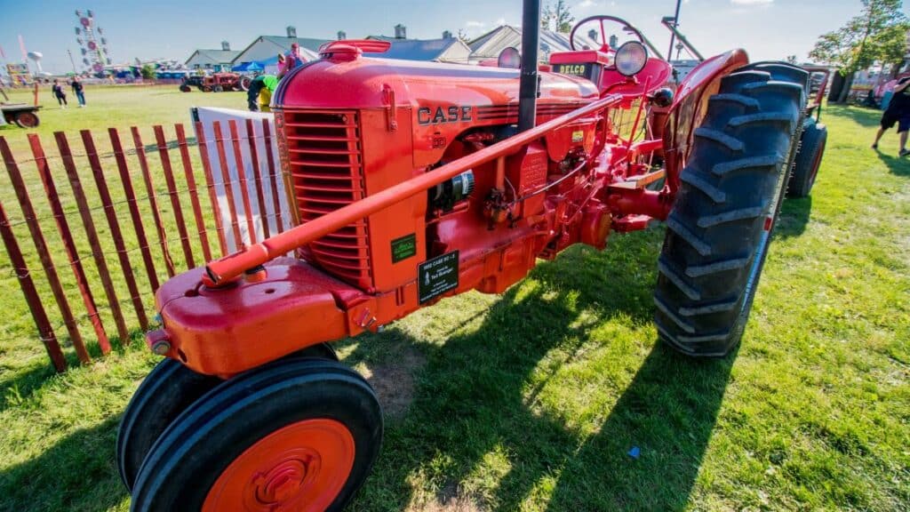 A classic red tractor on display at a rural farm fair under a bright blue sky.