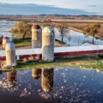 Aerial view of a flooded farm in Wabasha, MN, showcasing silos and barns in a rural landscape.