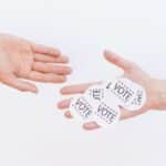 Close-up of hands exchanging vote stickers, symbolizing engagement in democratic election.