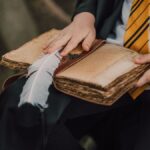 A child in a wizard costume reading an ancient spell book outdoors using a feather quill.