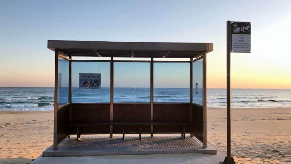 Bus stop on a sandy beach with ocean view at sunrise, creating a peaceful scene.