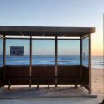 Bus stop on a sandy beach with ocean view at sunrise, creating a peaceful scene.