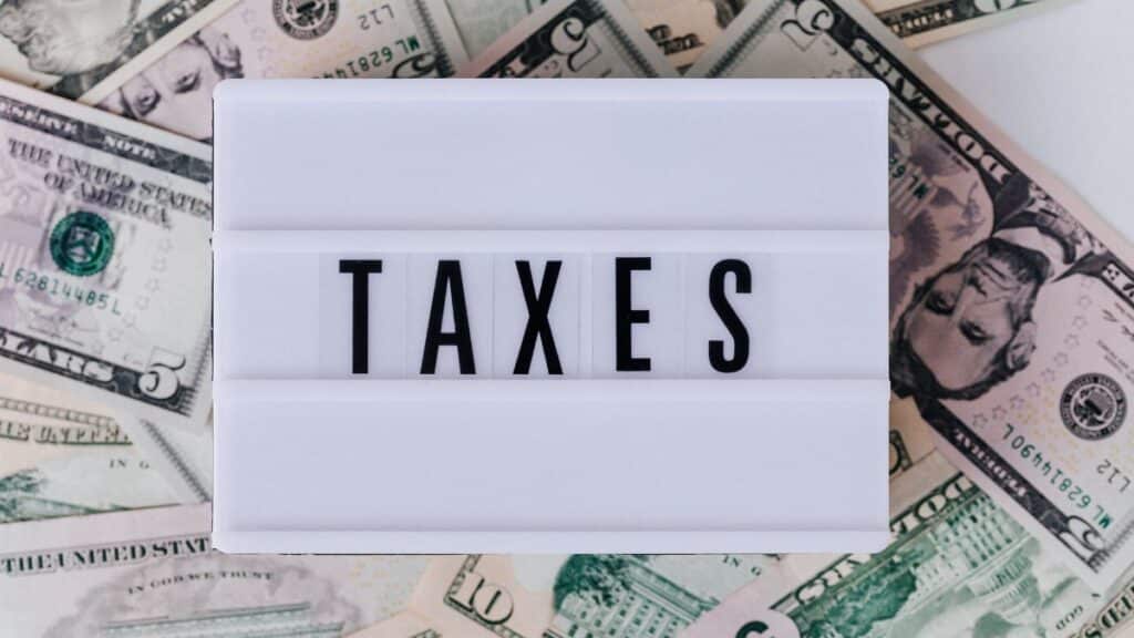Top view of white vintage light box with TAXES inscription placed on stack of USA dollar bills on white surface