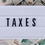 Top view of white vintage light box with TAXES inscription placed on stack of USA dollar bills on white surface