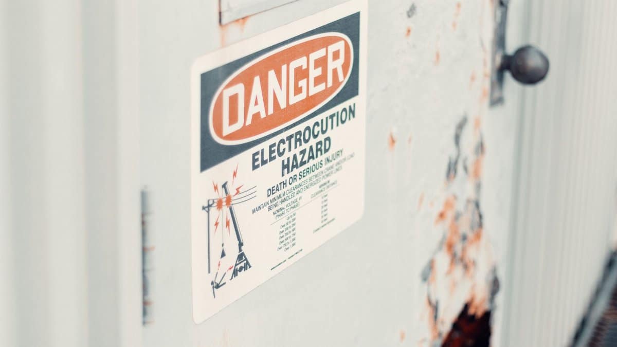 Close-up of a danger sign warning of electrocution hazard on a rusty utility door, indicating safety precautions.