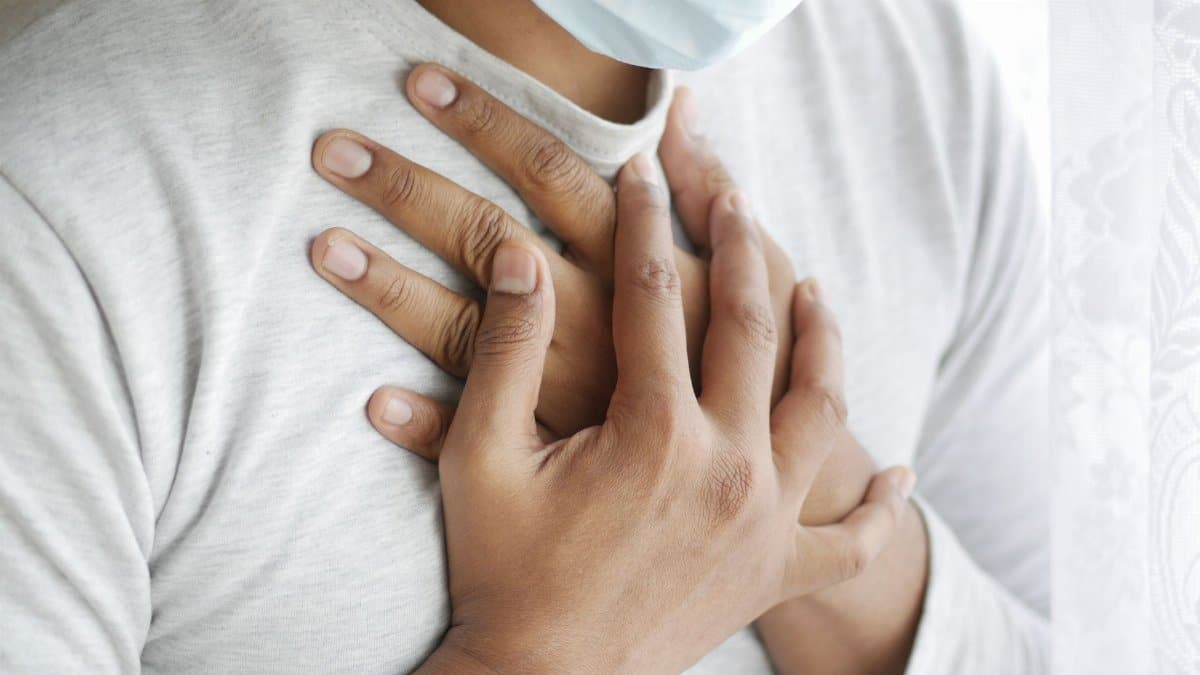 Close-up image of a masked person holding chest, symbolizing health concerns.