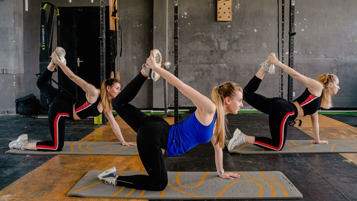 Three women practicing yoga poses on mats inside a fitness studio, promoting flexibility and well-being.