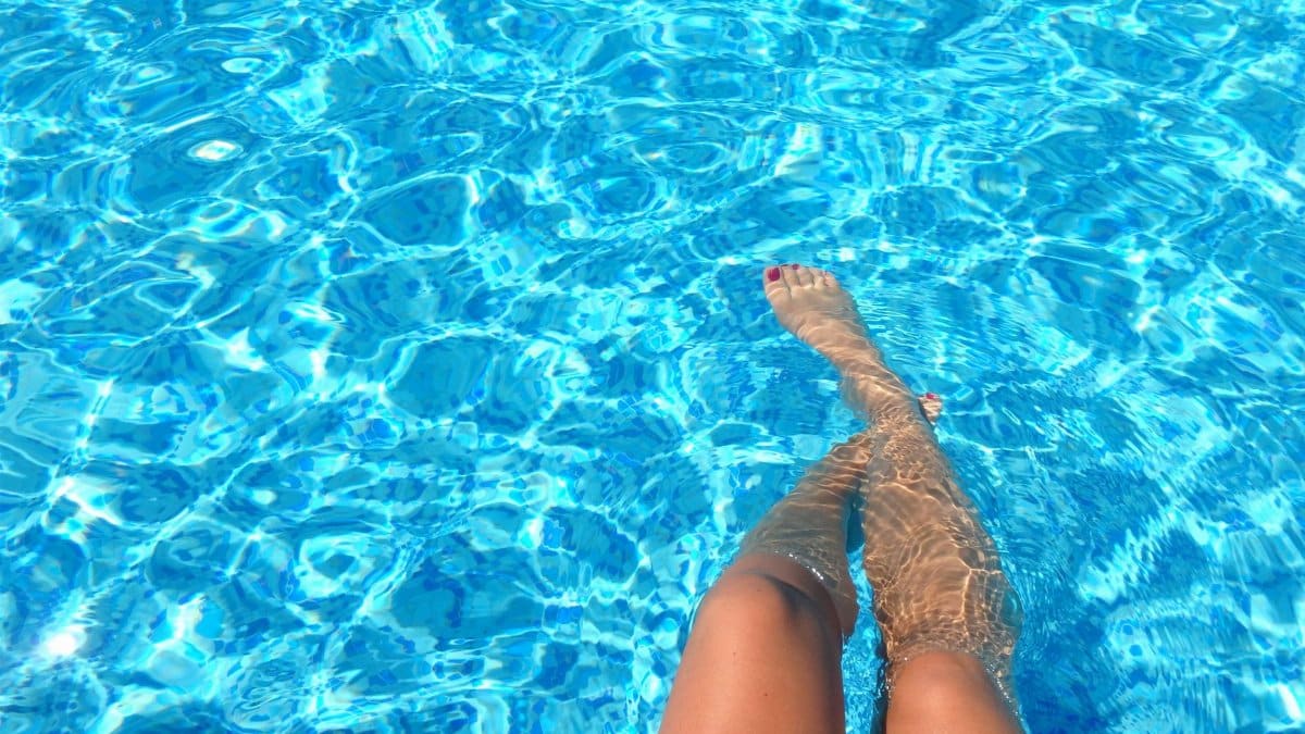 A person relaxes in a swimming pool with clear blue water, capturing summer vibes.