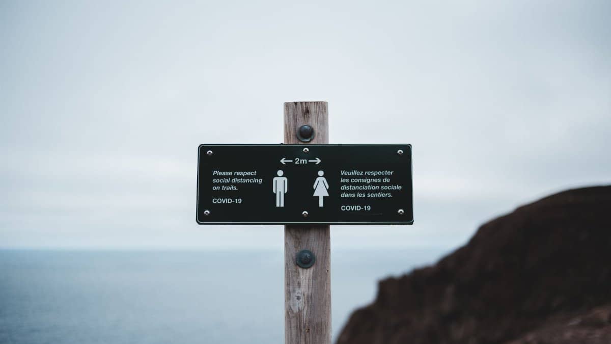 COVID-19 social distancing sign on a coastal trail emphasizes safety precautions during the pandemic.