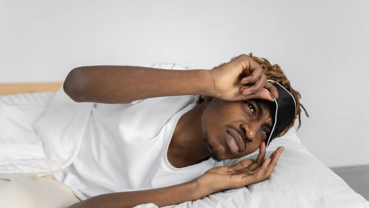 Young man removes sleep mask, starting his day in bed, indoors.