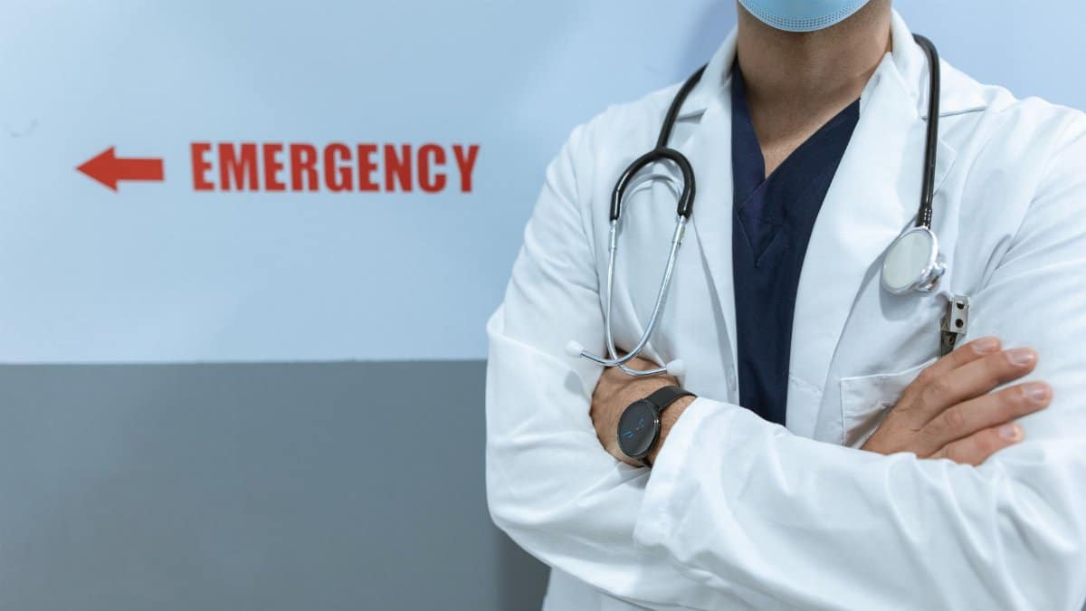Healthcare worker in emergency room with stethoscope and facemask, cross-armed posture.