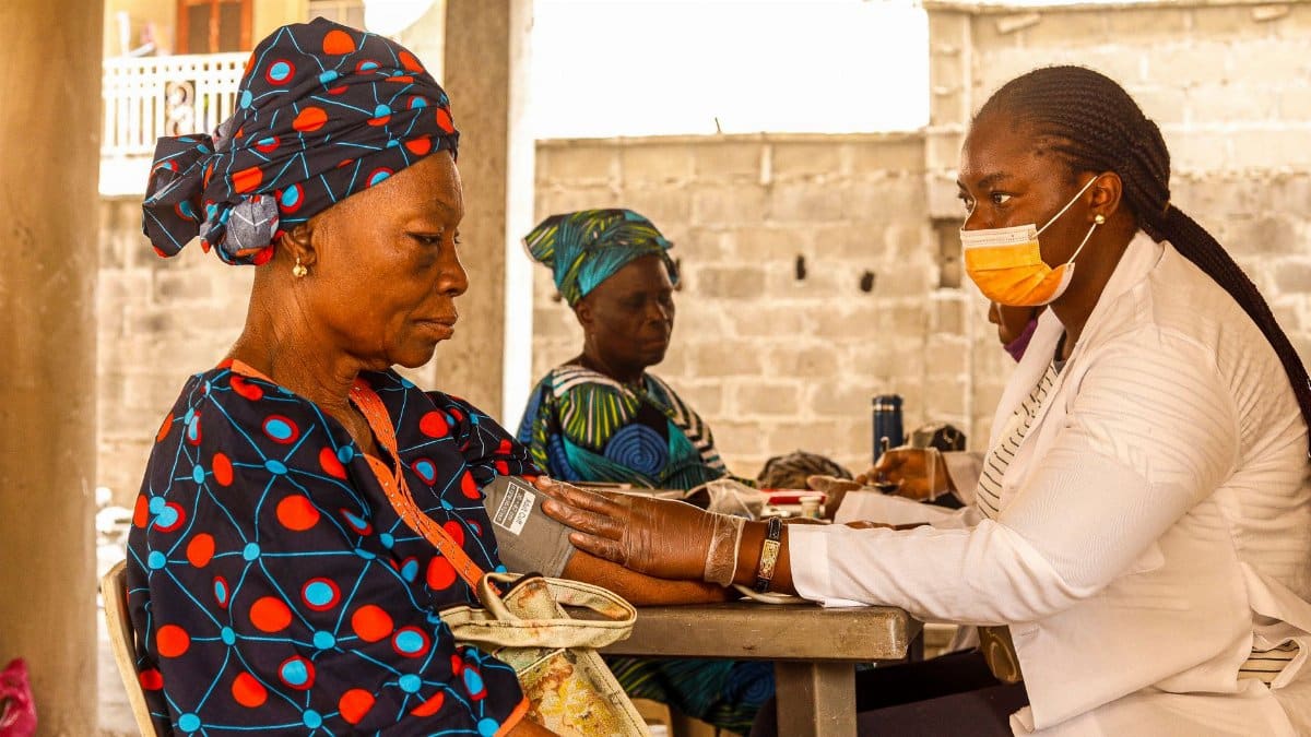 A healthcare worker checks blood pressure of an elderly woman in a rural clinic setting.