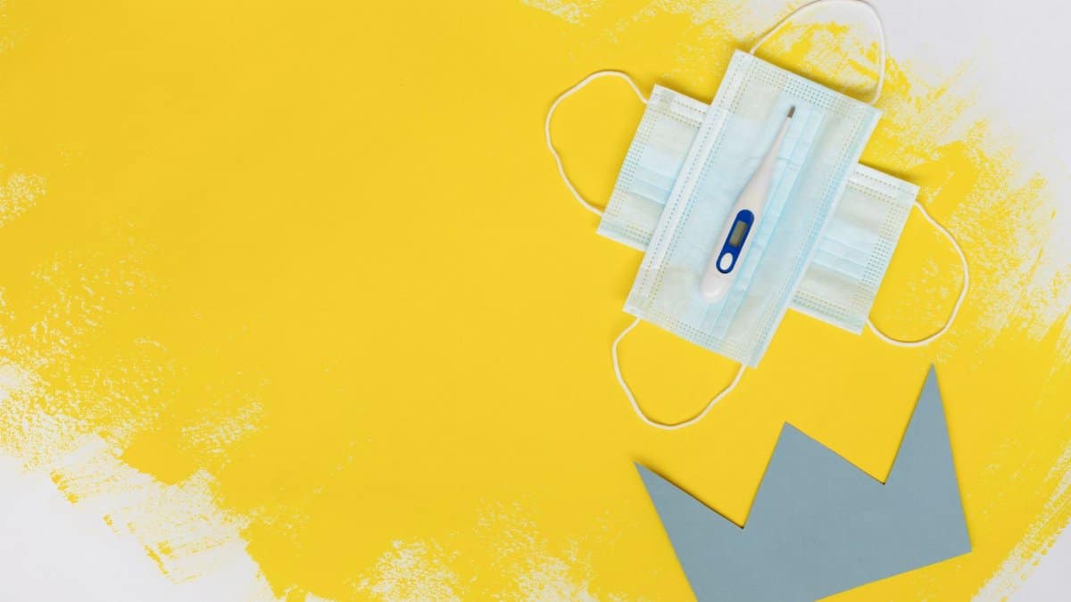 Digital thermometer on face masks with crown cutout on yellow background, symbolizing health and safety.