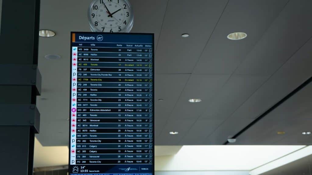 Airport departure screen showing various flight schedules and times with a wall clock above.