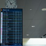 Airport departure screen showing various flight schedules and times with a wall clock above.
