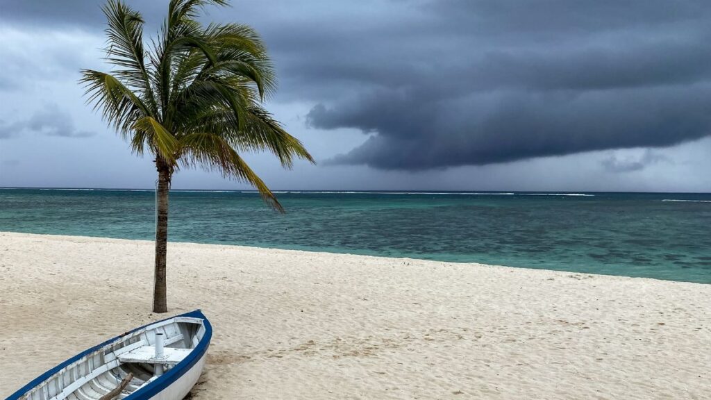 A lonely boat on a windy beach with palm trees and storm clouds gathering at Le Morne, Mauritius.