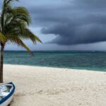 A lonely boat on a windy beach with palm trees and storm clouds gathering at Le Morne, Mauritius.
