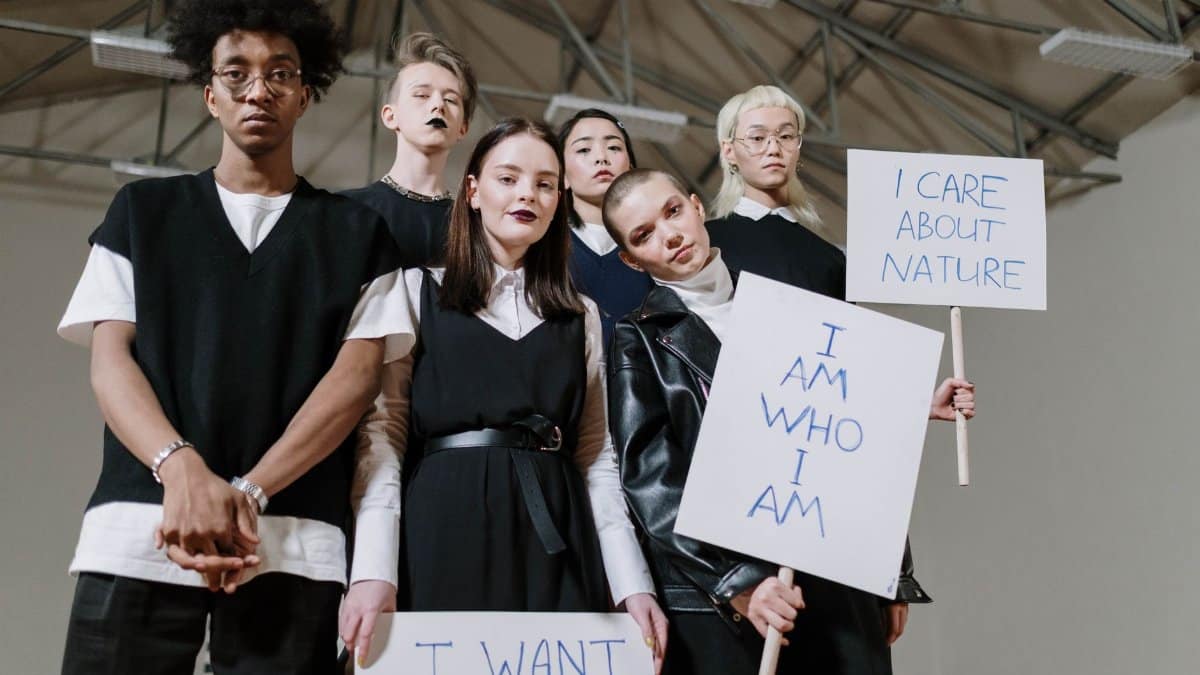 A diverse group of teenagers holding protest signs indoors, advocating individuality and environmental care.