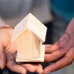 Hands holding a small wooden house model, symbolizing new home ownership and real estate transactions.
