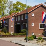 A picturesque suburban street in the Netherlands with Dutch flags displayed on brick houses during a sunny day.