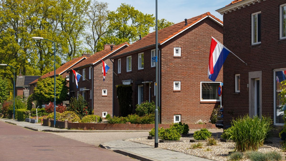 A picturesque suburban street in the Netherlands with Dutch flags displayed on brick houses during a sunny day.