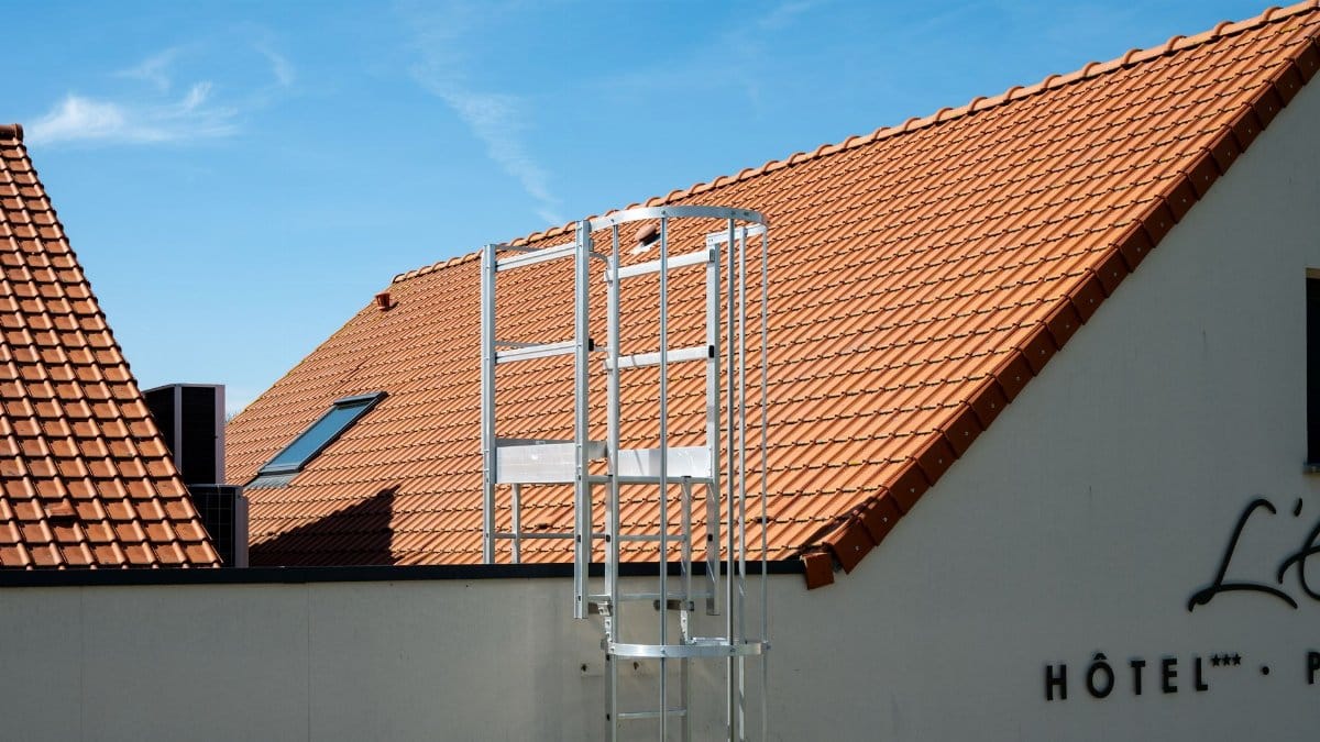 Sunny view of a hotel rooftop with ladder, featuring terracotta tiles and blue sky in Escalles, France.