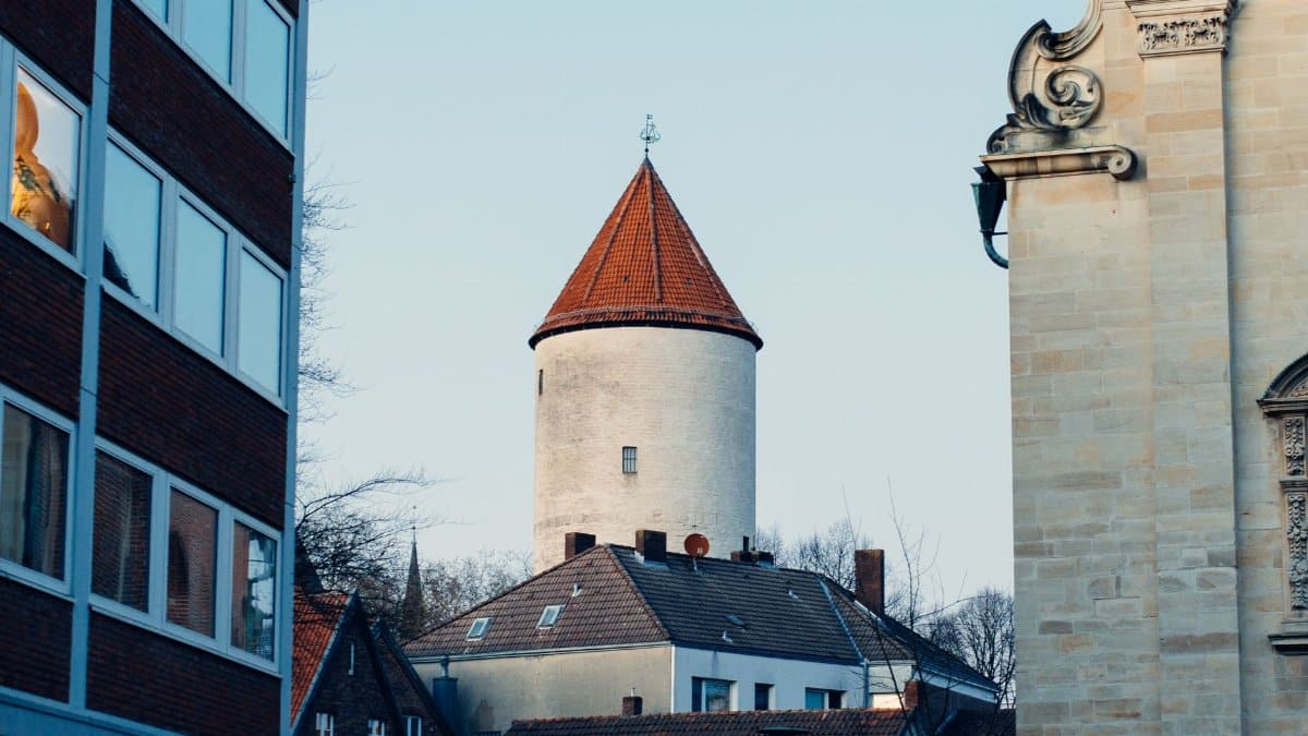 A historic tower framed by modern and classic buildings, suggesting a blend of old and new architecture.